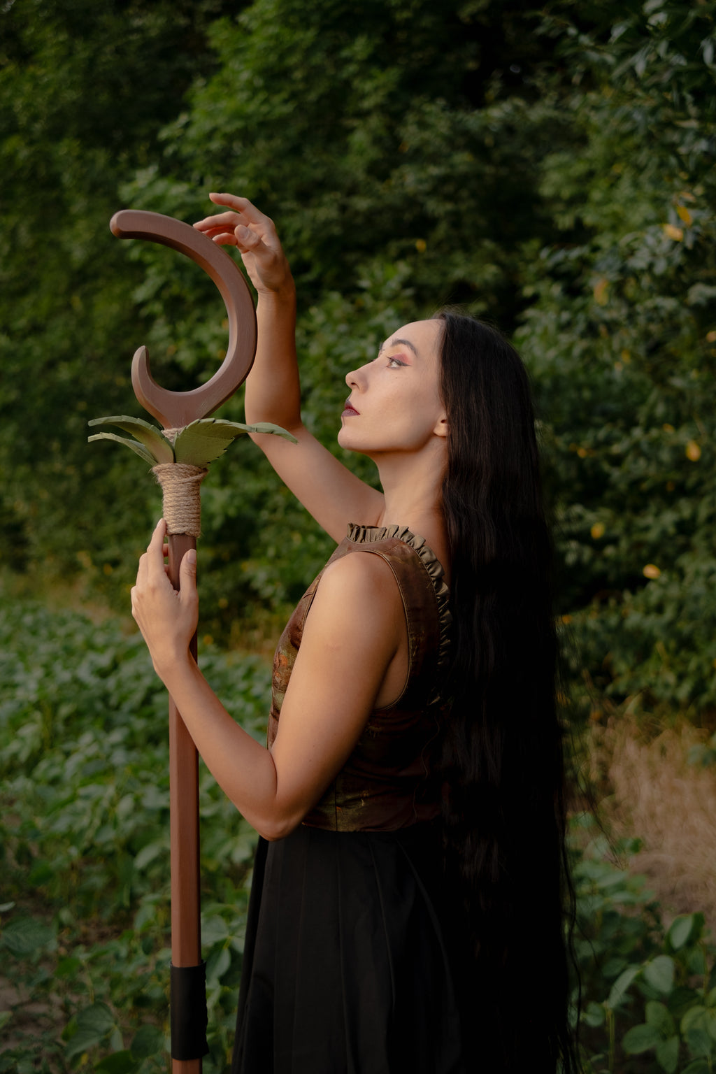 Leafbound Crescent staff held outdoors with natural forest greenery behind