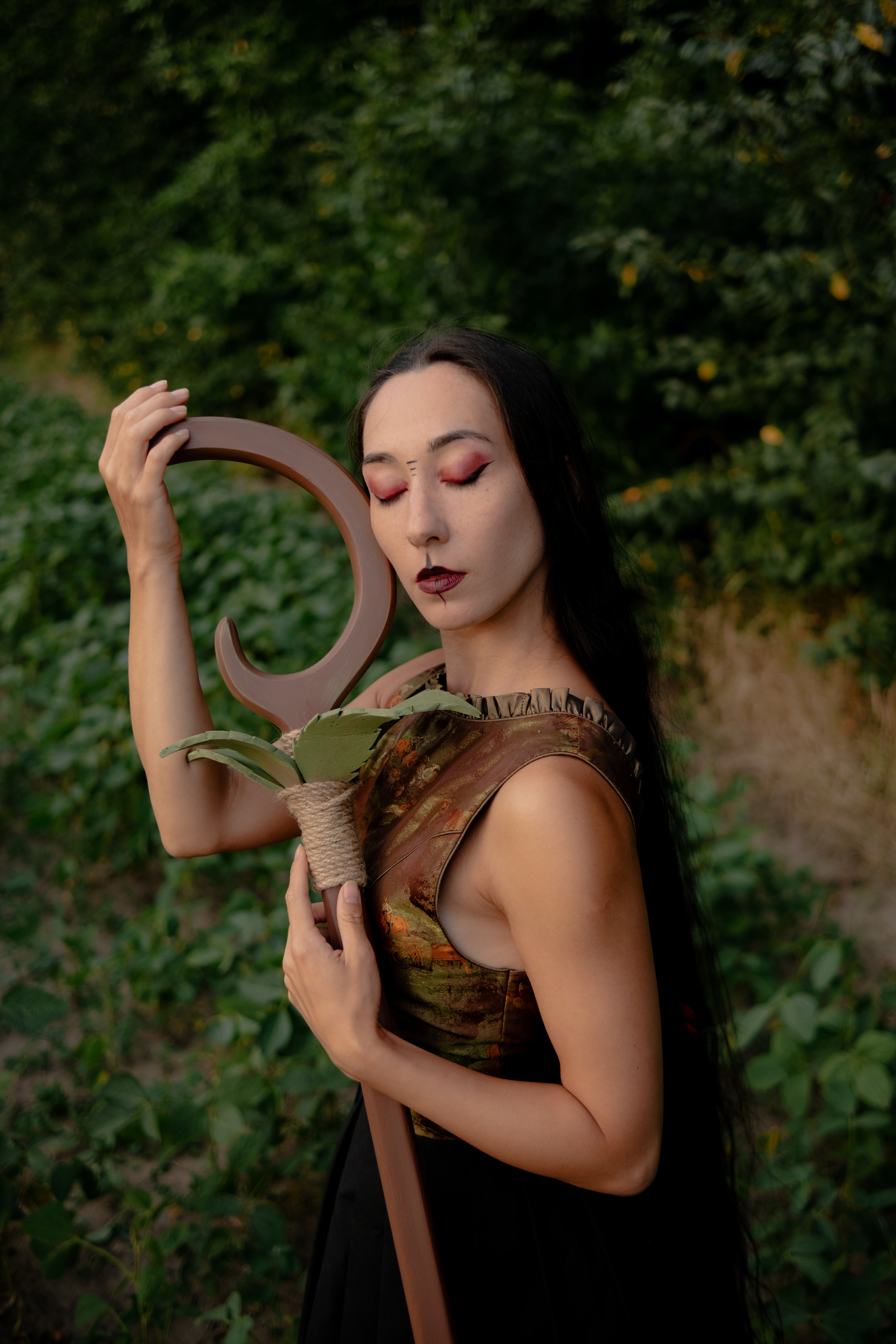 Model holding green leaf crescent fantasy staff in woodland costume styling