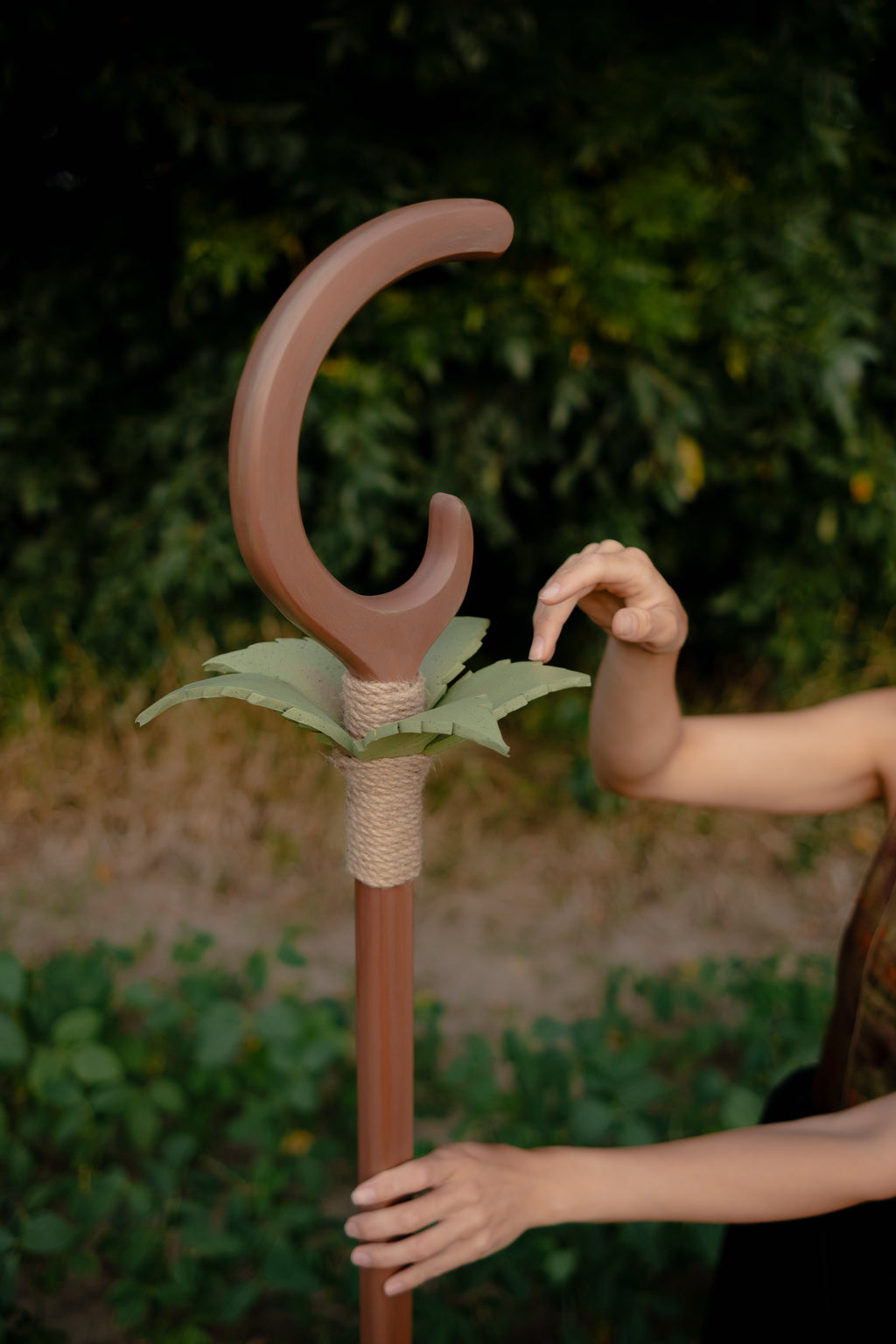 Close-up of hand holding wooden staff with crescent and leaf decoration