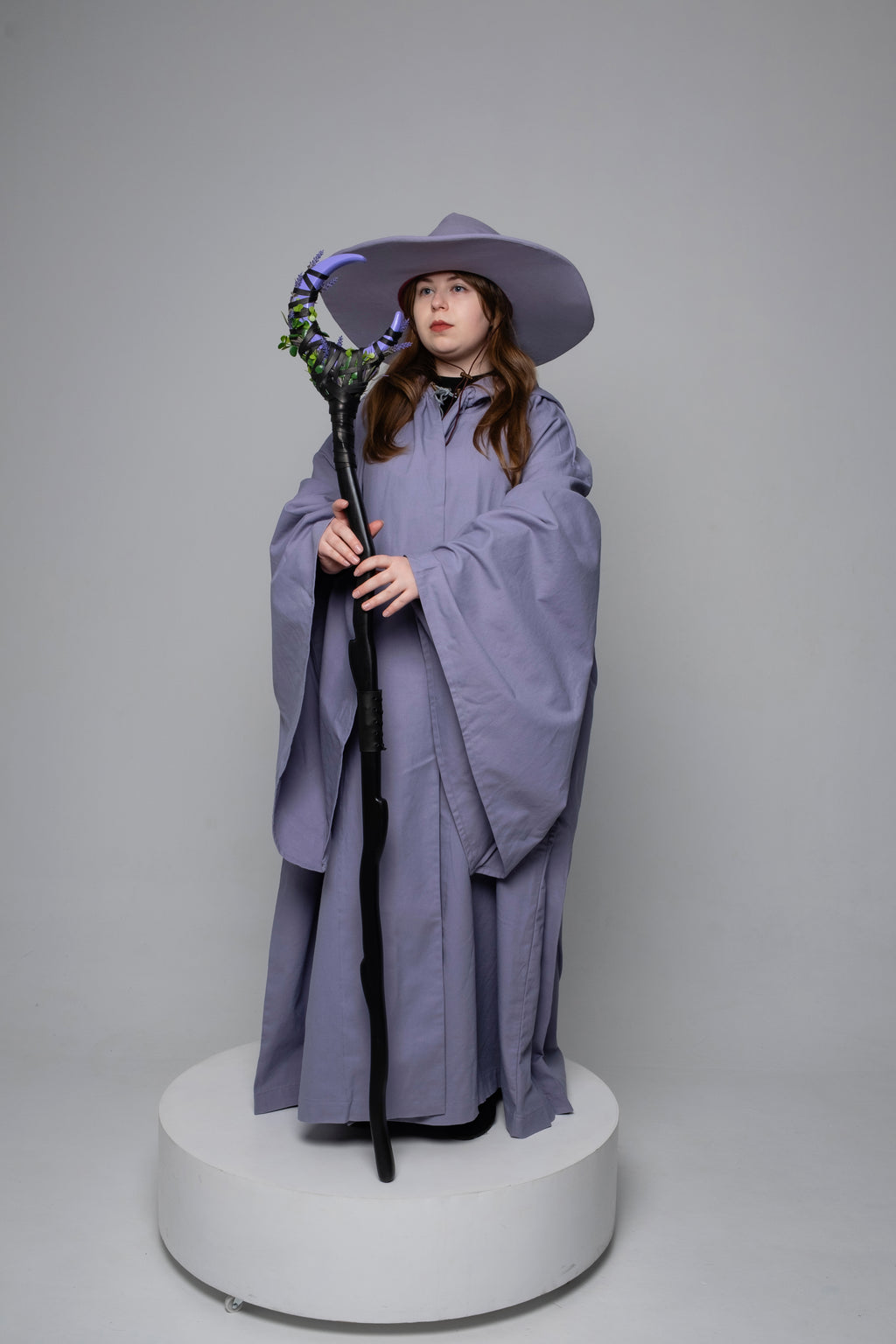 Person wearing a purple outfit with a hat and holding a lavender staff