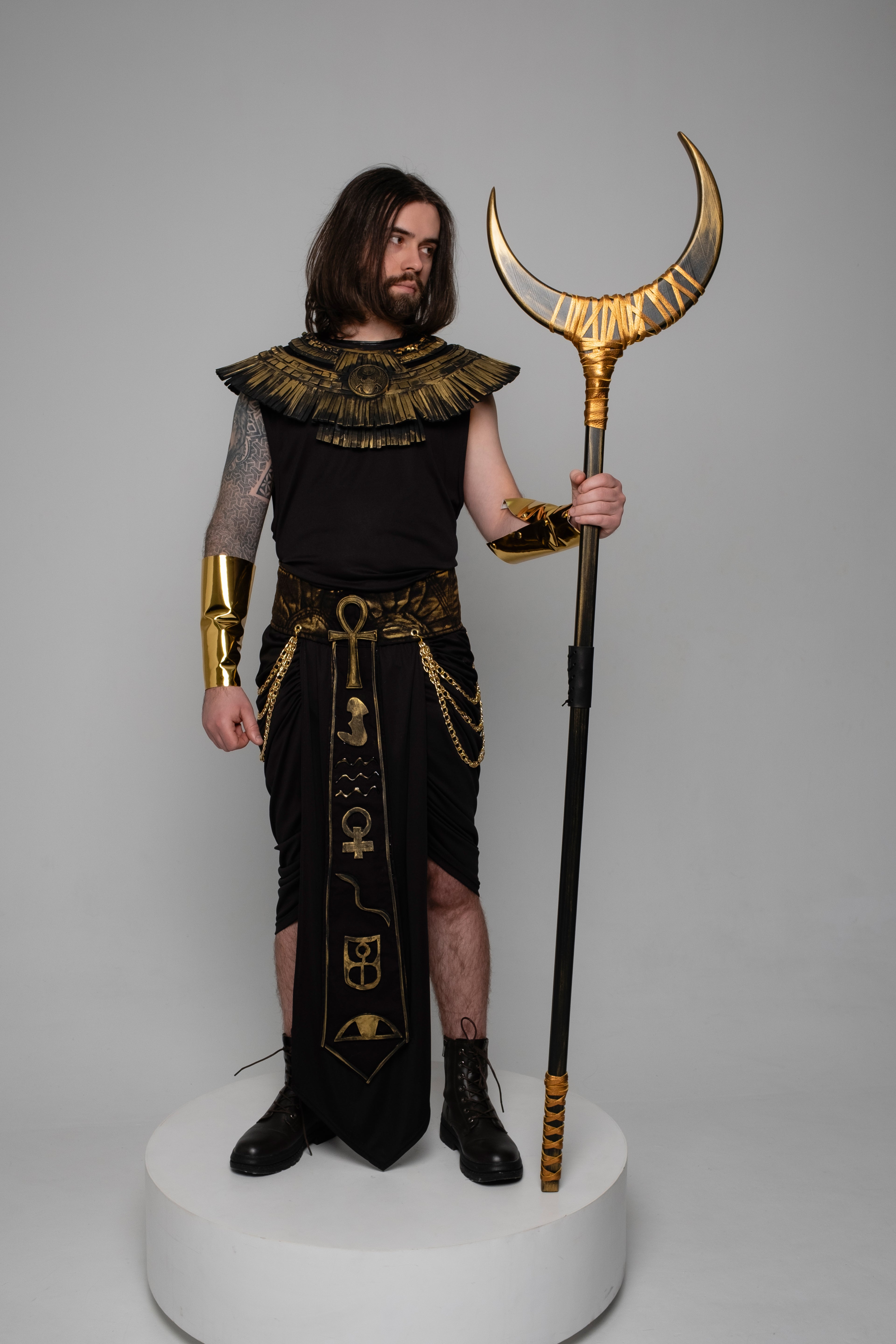 Person in Egyptian-themed costume holding a staff with a headdress on a gray background
