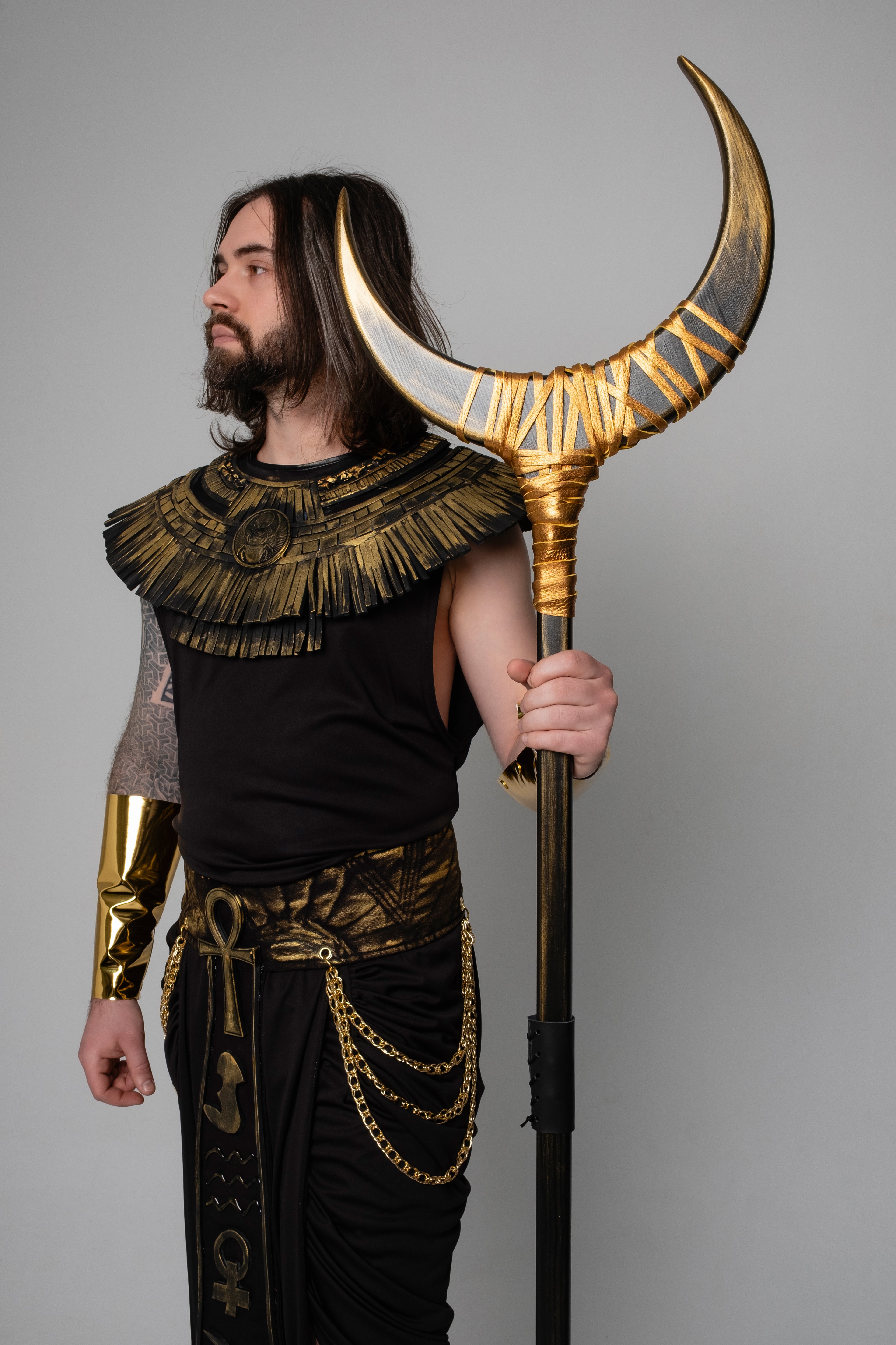 Person in Egyptian-style costume holding a staff with horns against a gray background