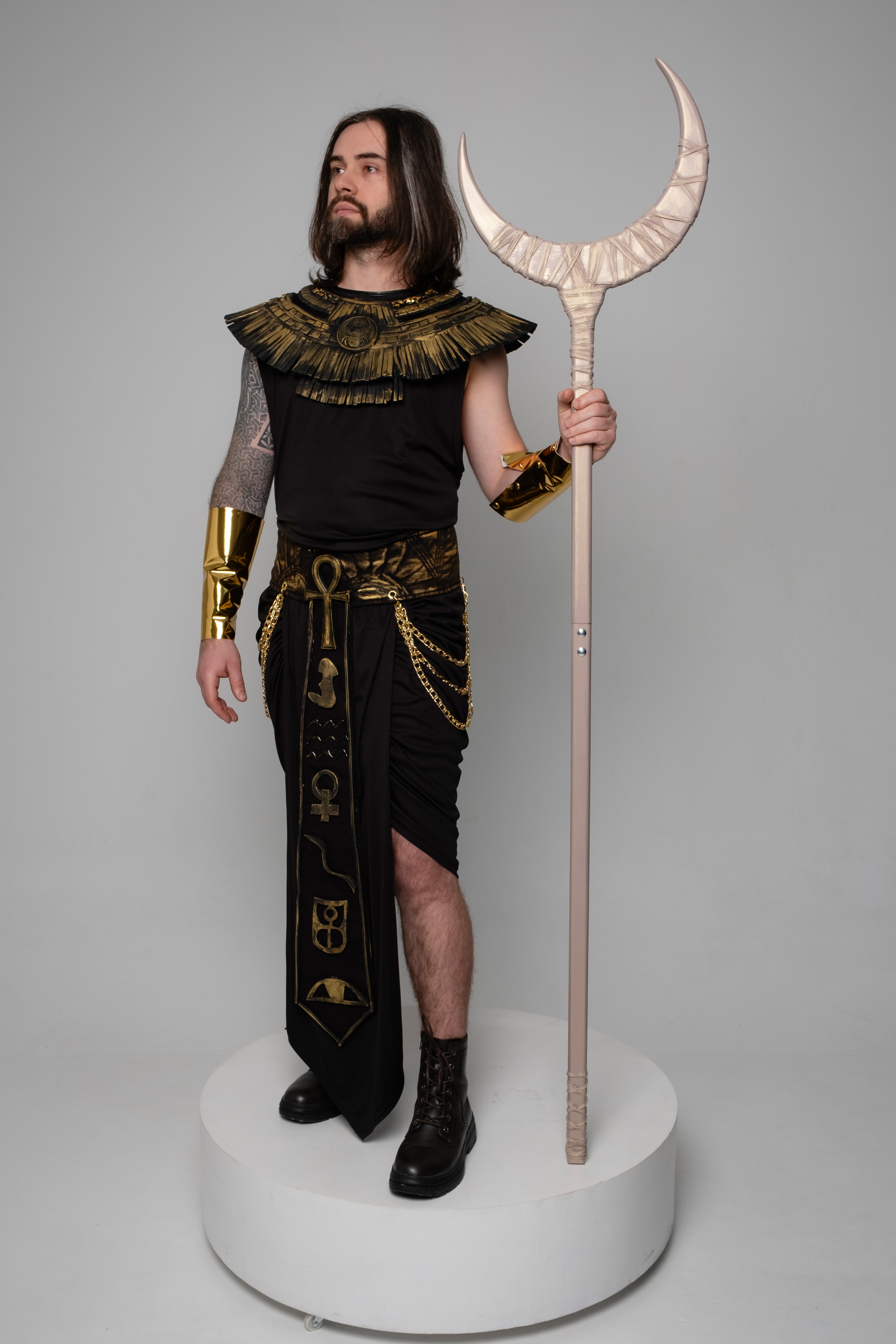 Person in Egyptian-style costume holding a staff on a gray background
