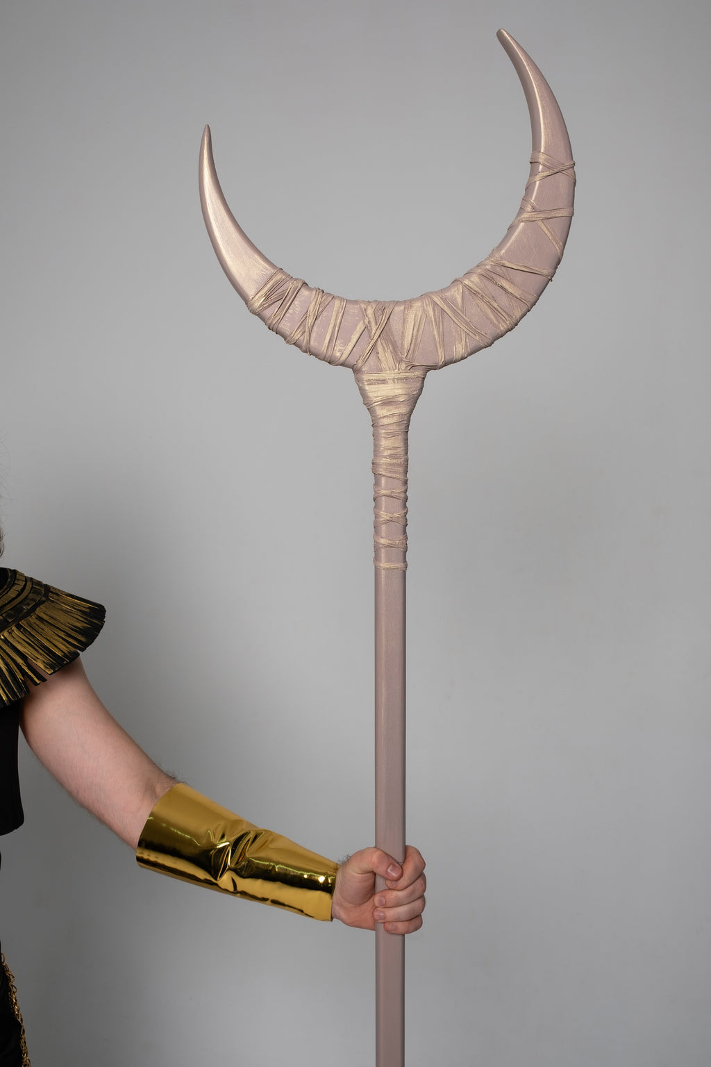 Person holding a large, decorative spear against a gray background