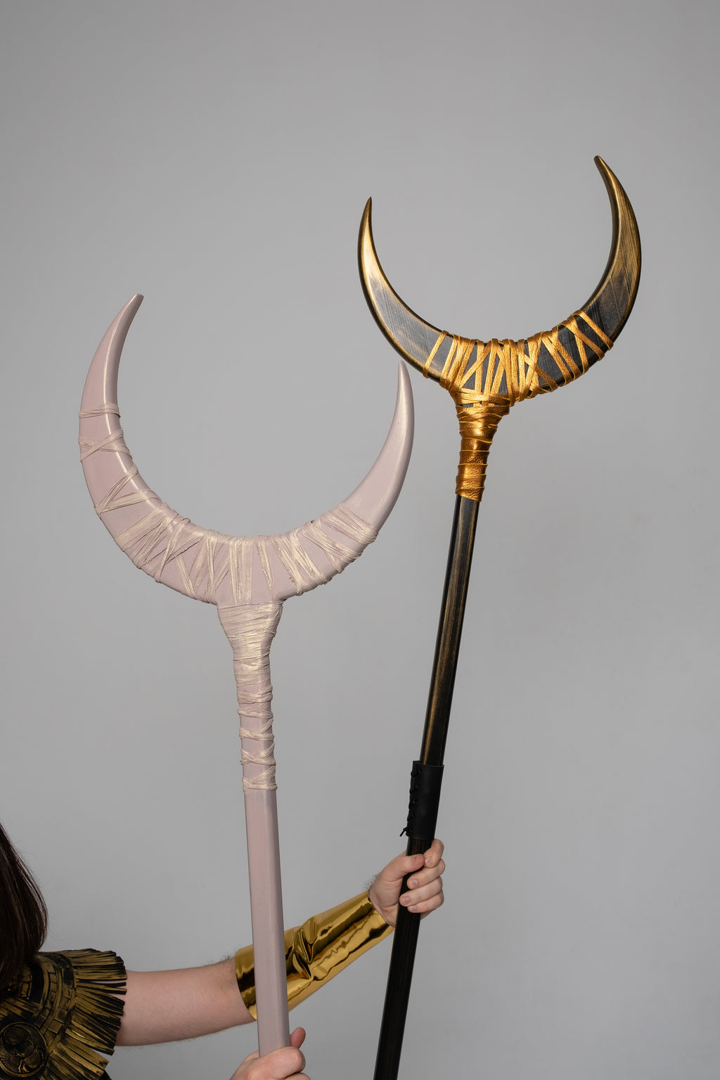 Two large decorative staffs with curved ends, one gold and one pink, held against a gray background.
