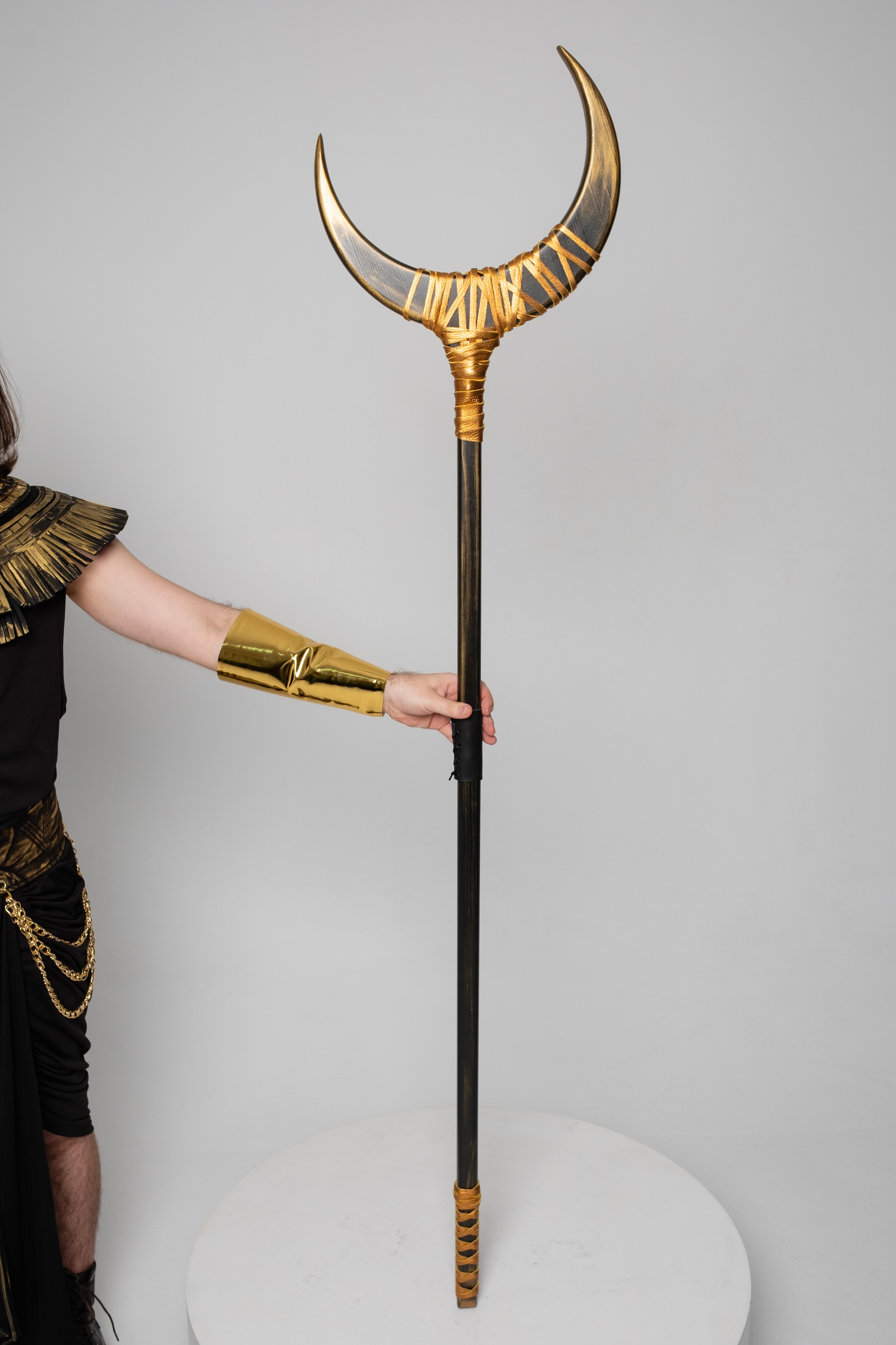 Person holding a large, ornate staff with a crescent moon design against a plain background