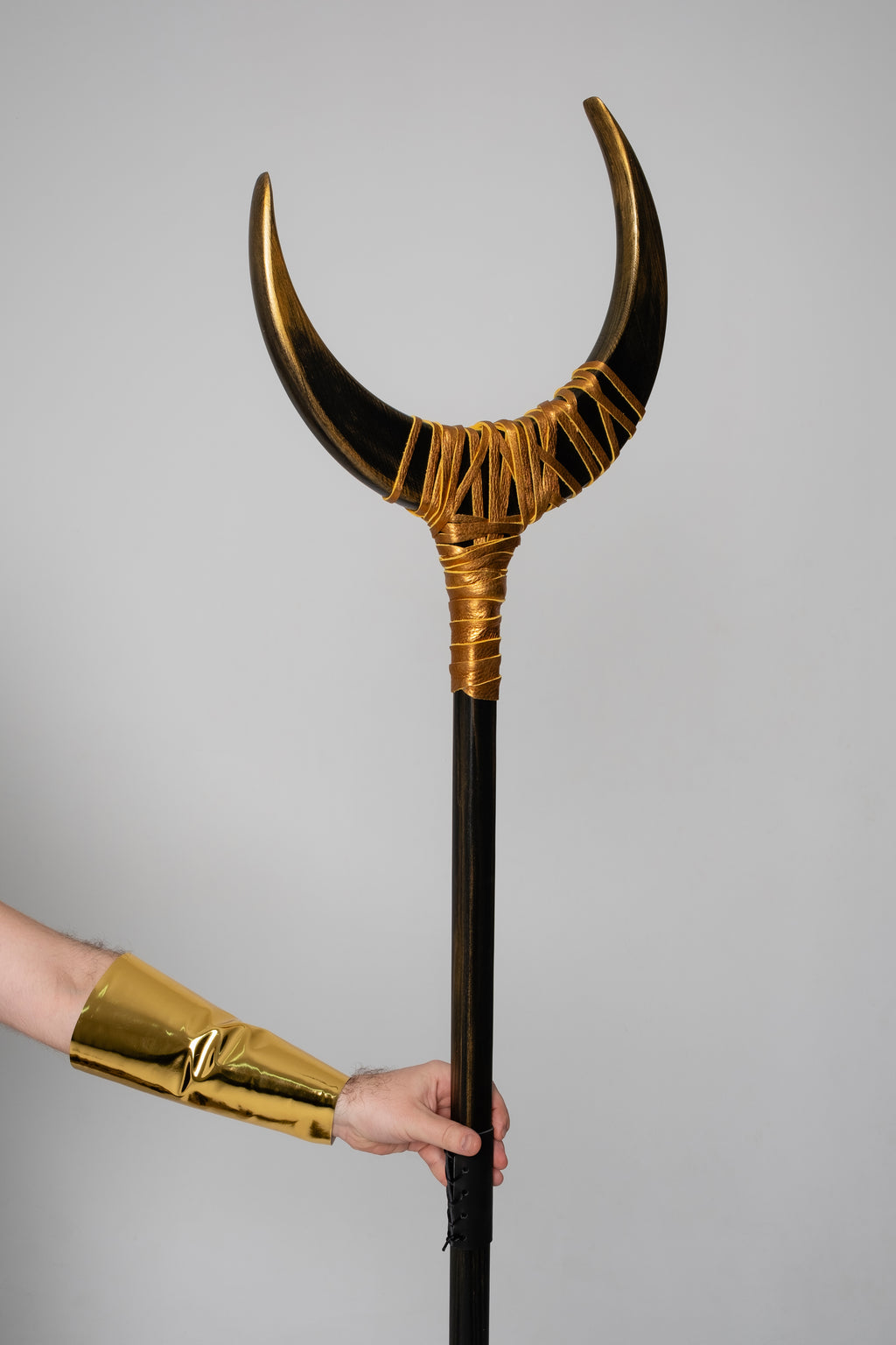 Decorative staff with gold accents held by a person wearing a gold arm sleeve against a gray background