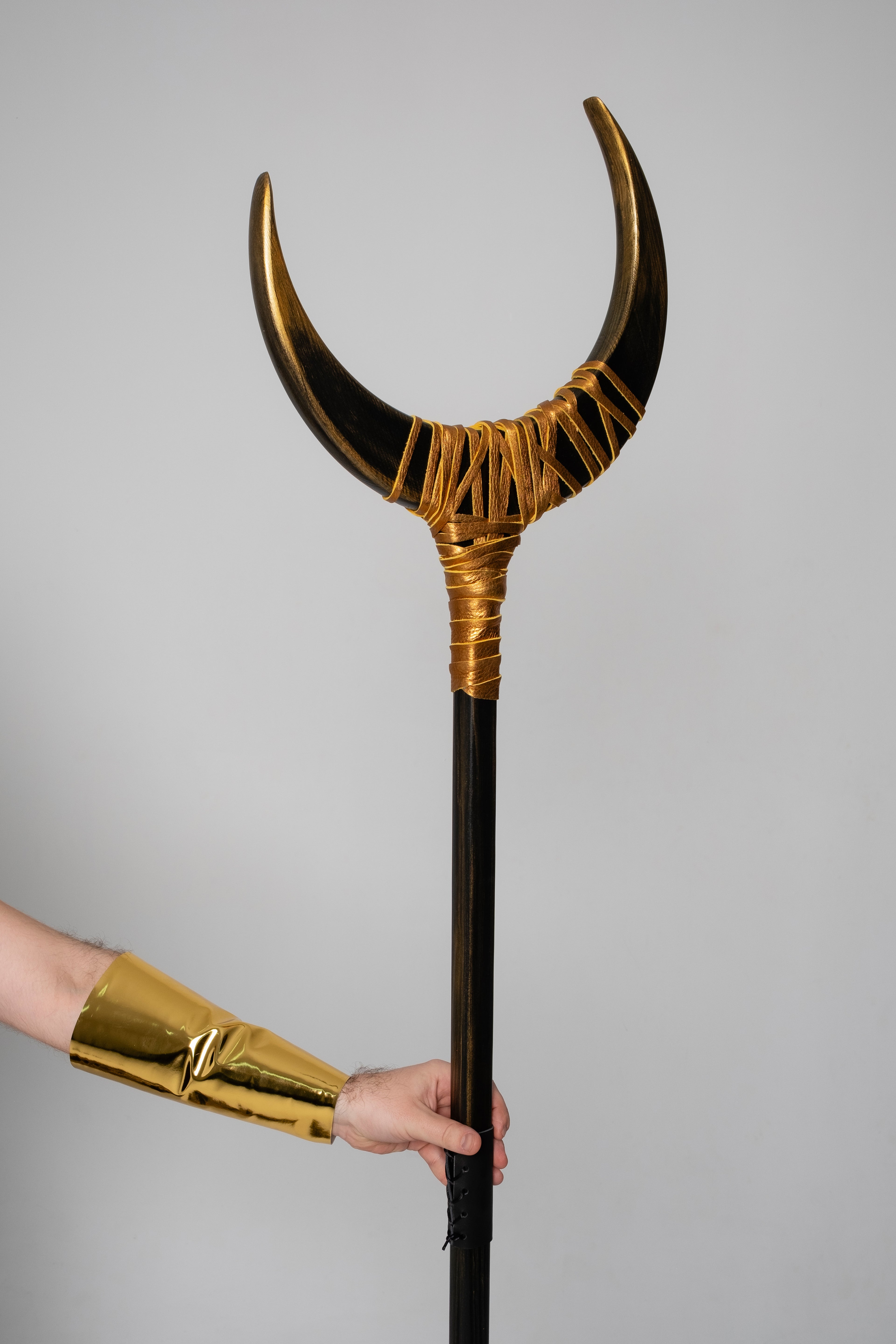 Decorative staff with gold accents held by a person wearing a gold arm sleeve against a gray background