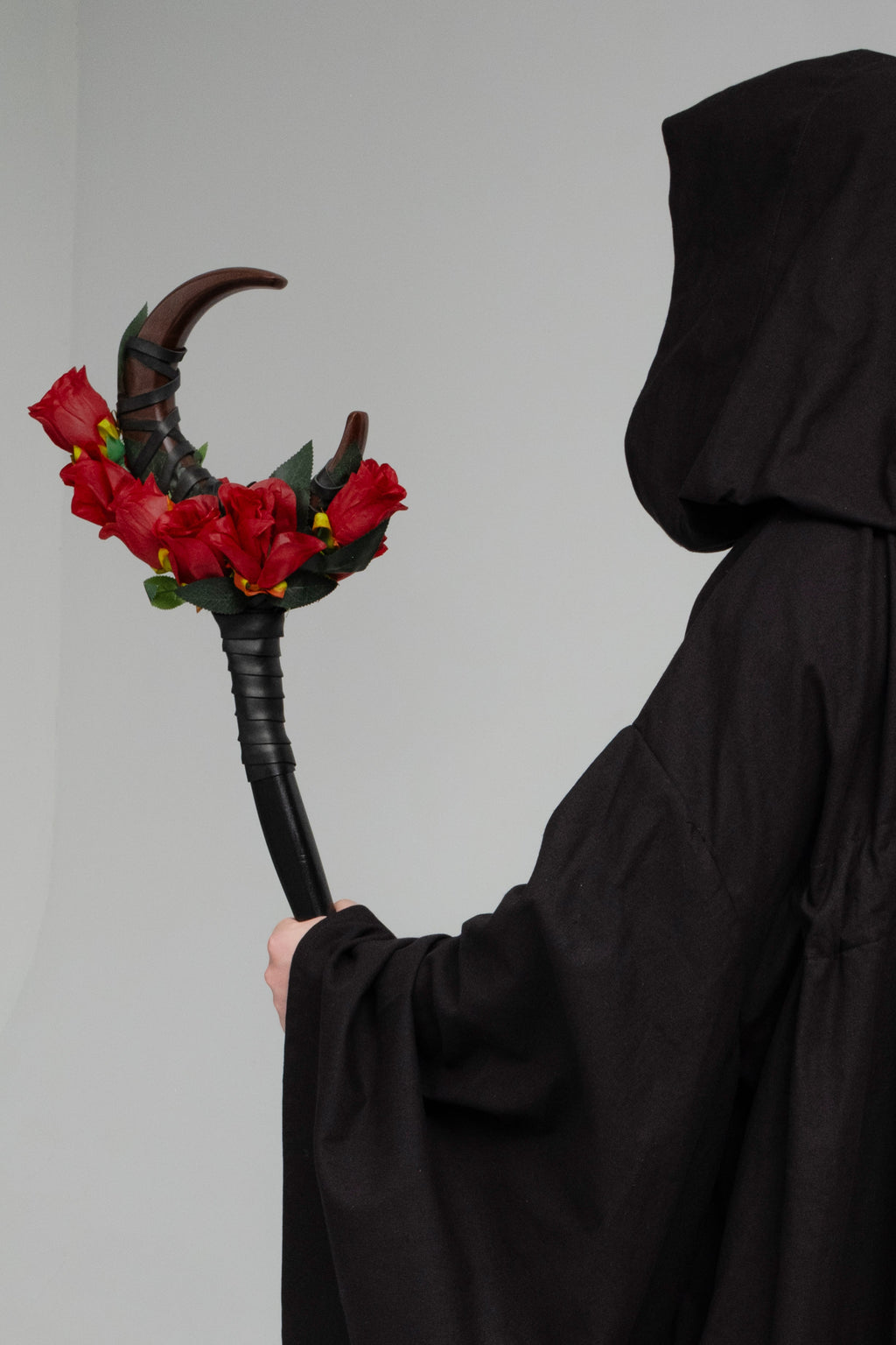 Person in a black hooded robe holding a staff with red roses 