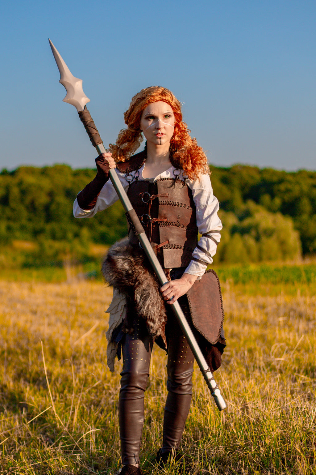 Person in medieval warrior costume holding a spear in a field with trees in the background