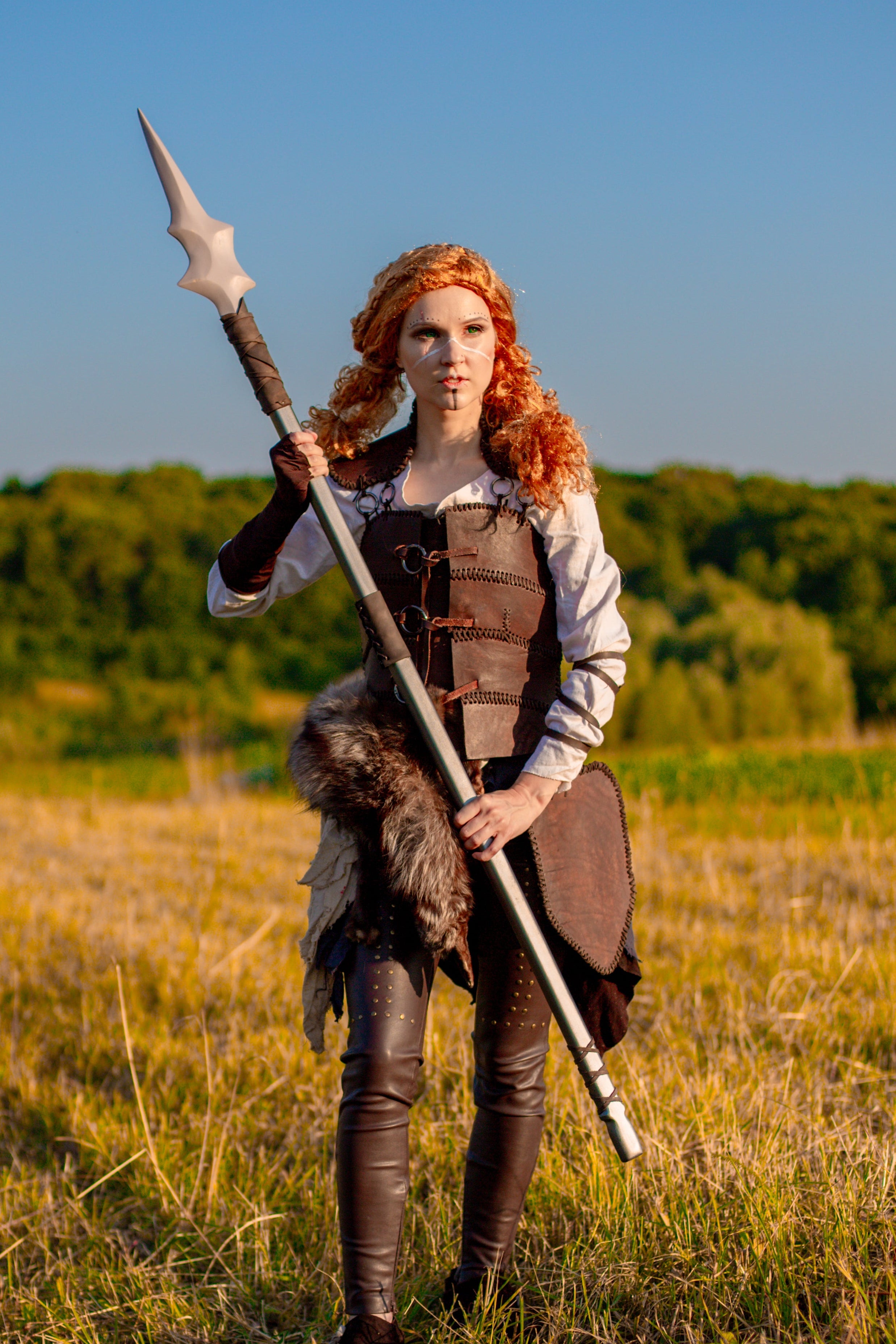 Person in medieval warrior costume holding a spear in a field with trees in the background