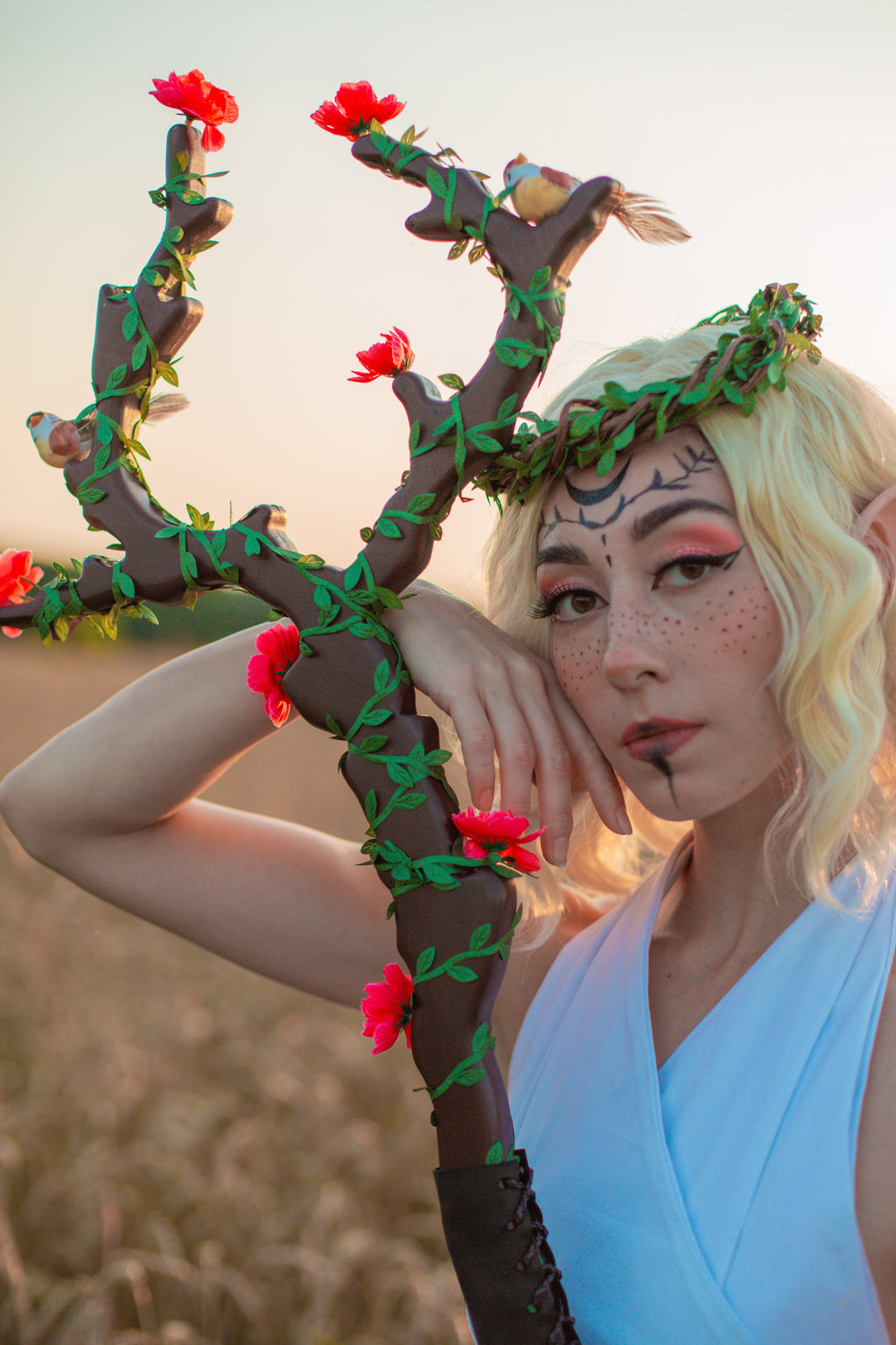 Person in elf costume holding a decorative branch with flowers against a blurred natural background