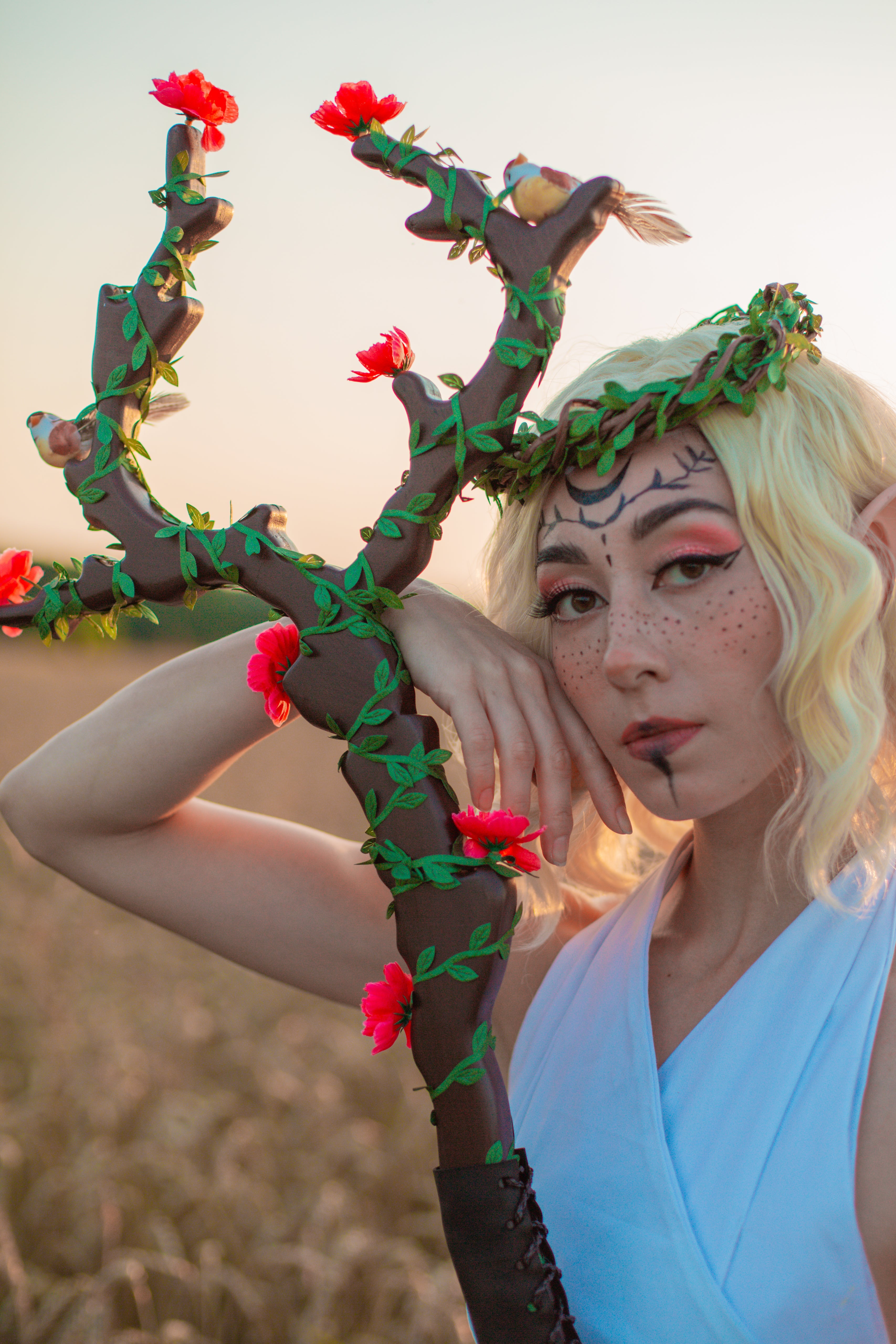 Person in elf costume holding a decorative branch with flowers against a blurred natural background