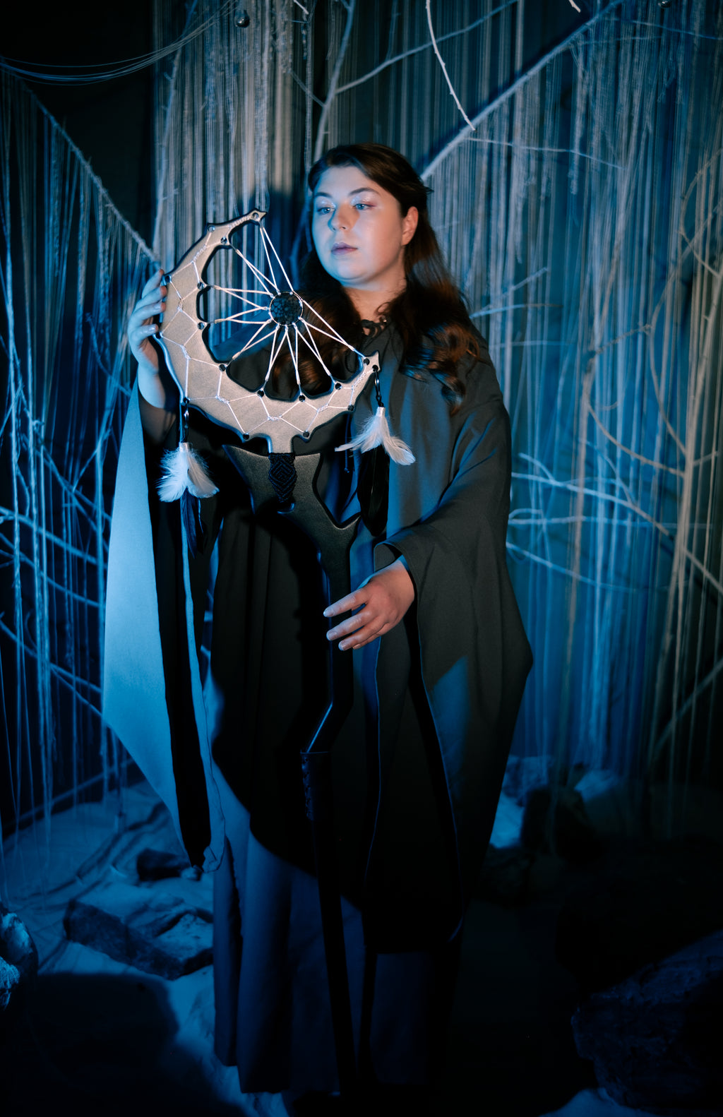 Person holding a dreamcatcher in a dark, forest-like setting