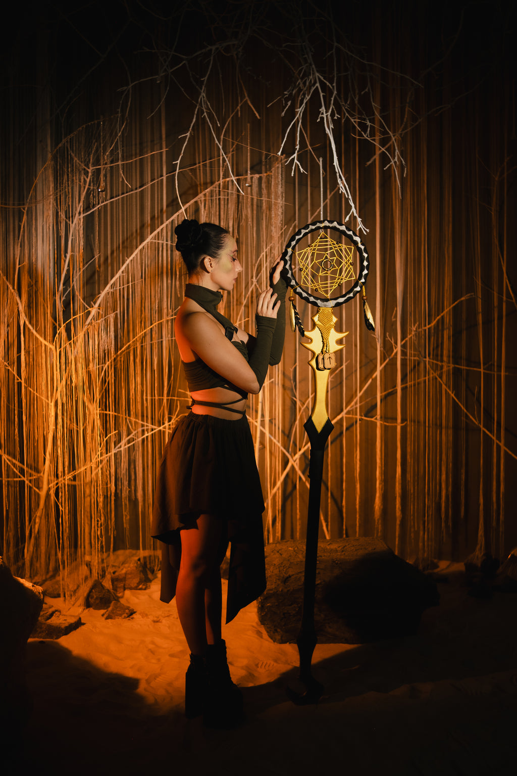 Person holding a large dreamcatcher in a dark, forest-like setting with warm lighting.
