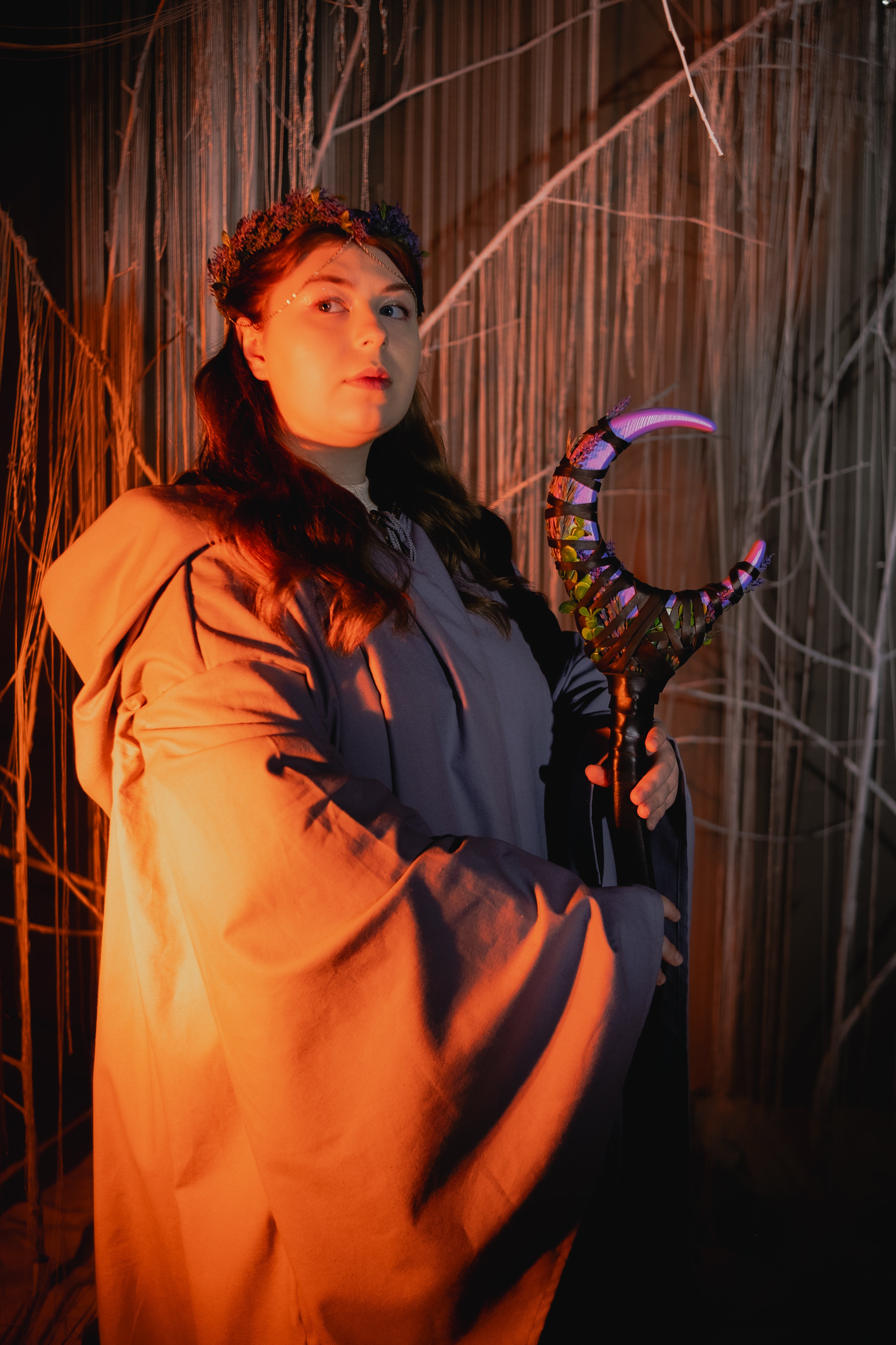 Person in a beige coat holding a colorful staff against a textured wall.