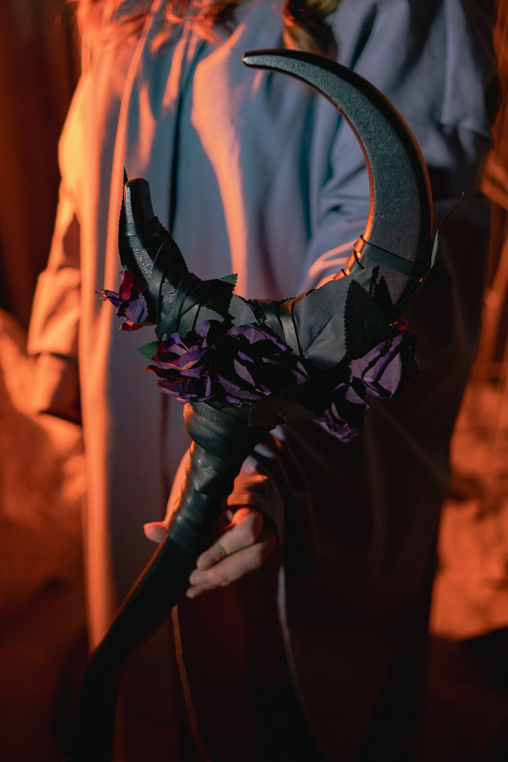Person holding a black scythe with decorative elements against a blurred background