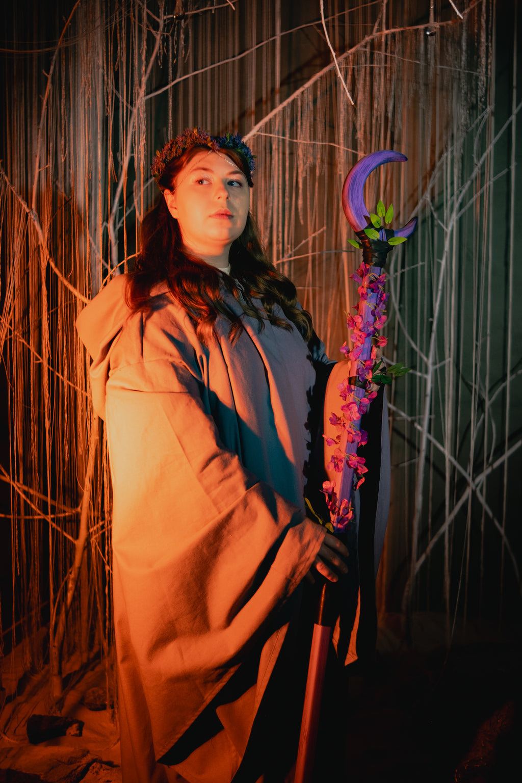 Person in a costume holding a staff with flowers against a dark background