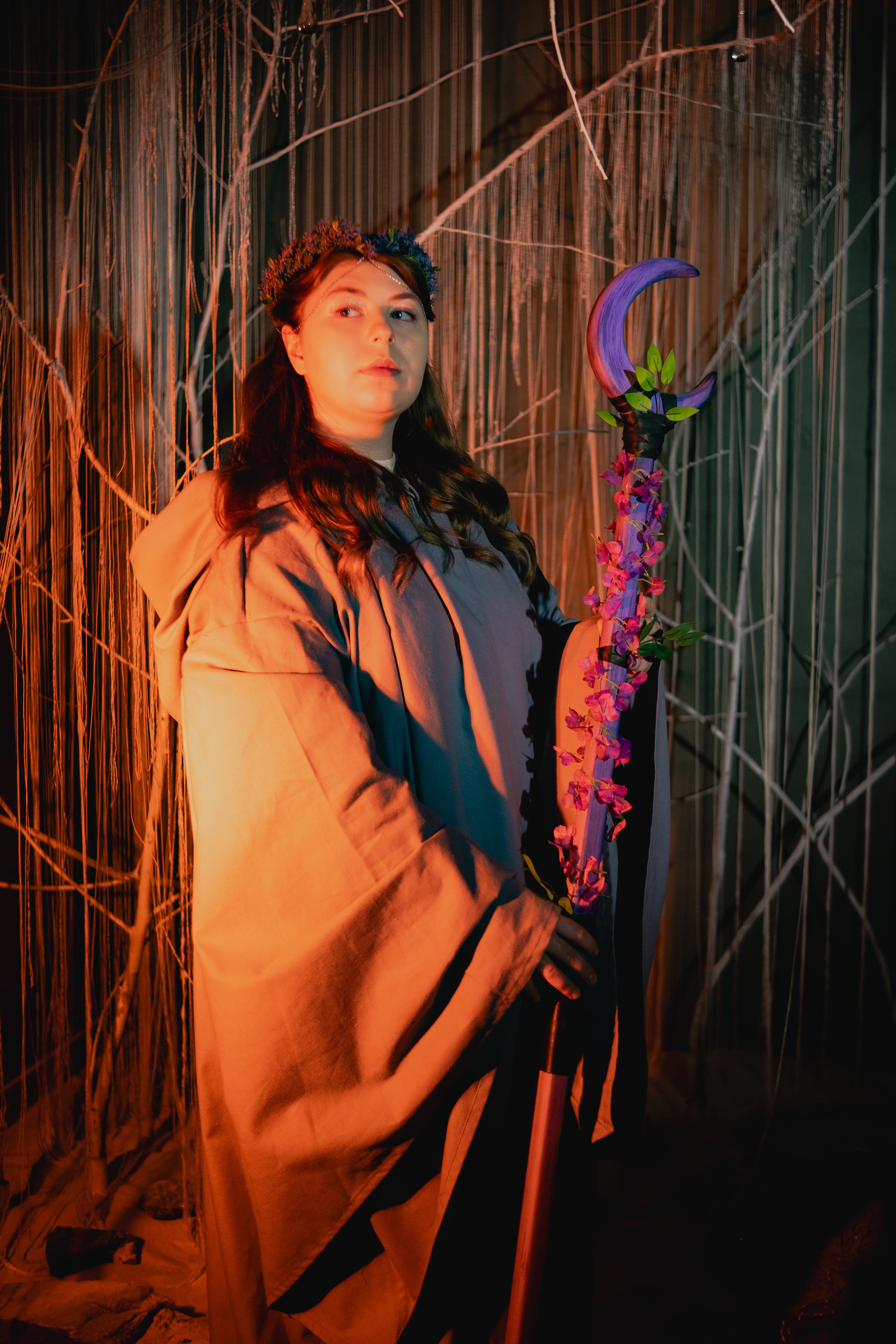 Person in a costume holding a staff with flowers against a dark background
